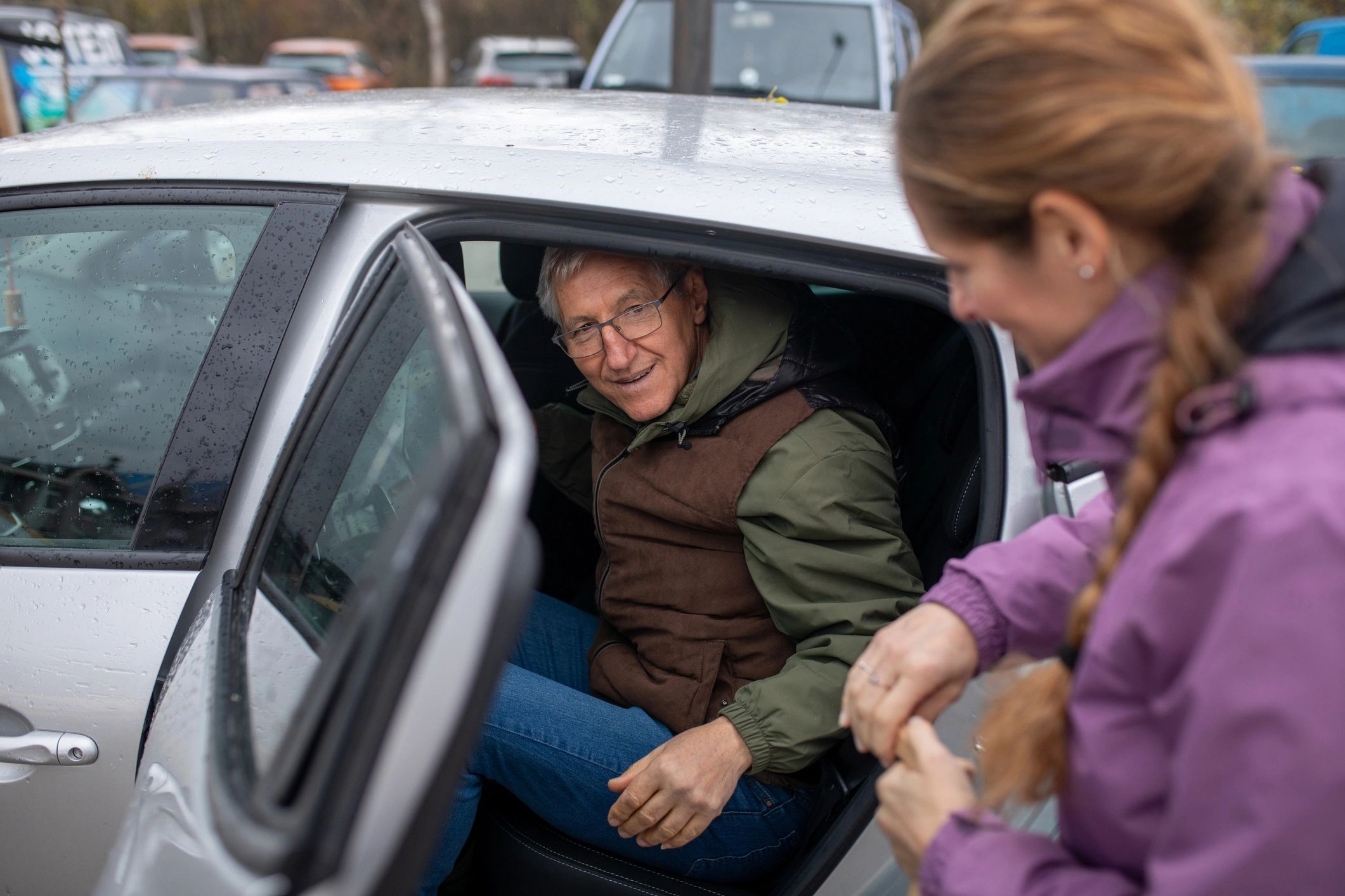 Caregiver helping a senior man get into a car